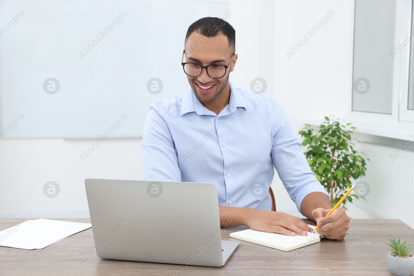 Photo of Happy young intern working with laptop at table in modern office