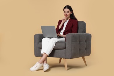 Photo of Confused woman with laptop sitting in armchair on beige background