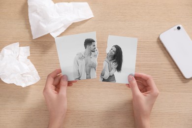 Divorce and breakup. Woman holding parts of ripped black and white photo at table, top view