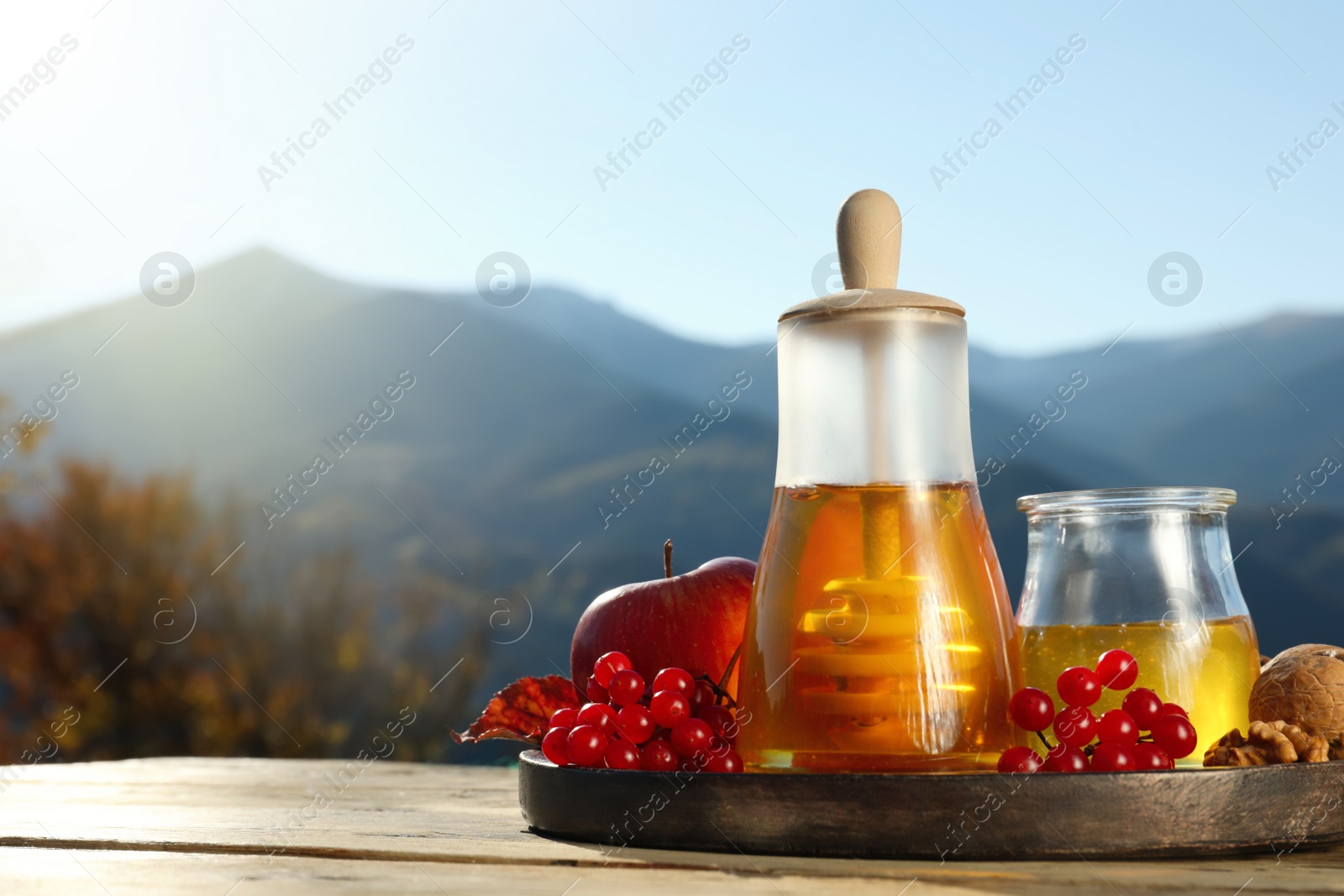 Photo of Fresh aromatic honey, rowan berries, apples and nuts on wooden table against mountain landscape. Space for text