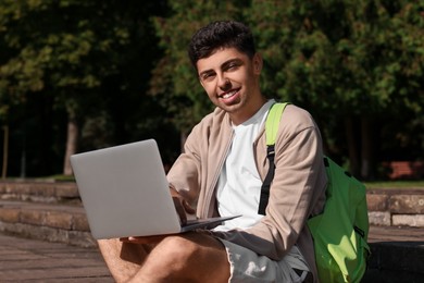 Photo of Happy young student studying with laptop on steps in park