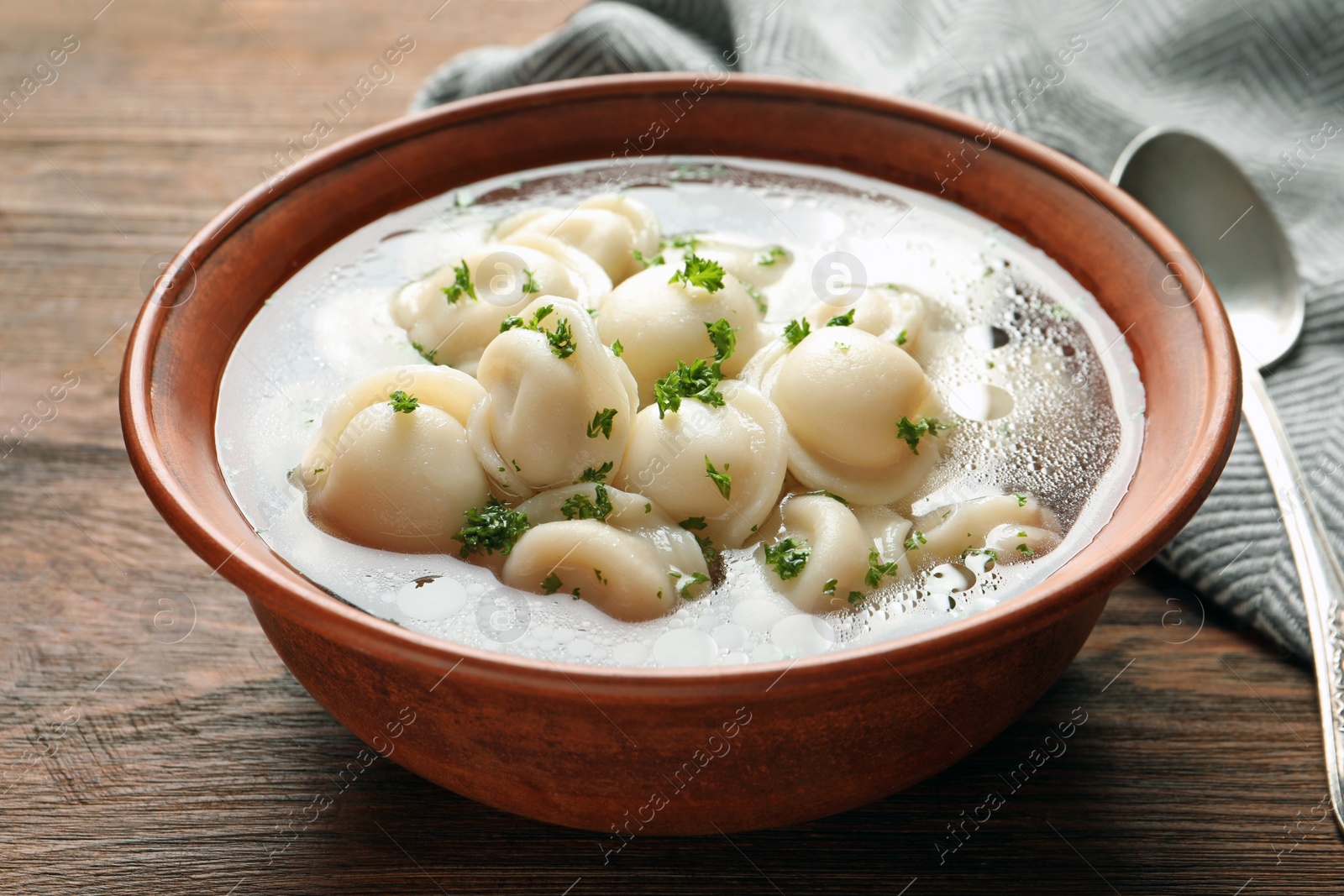 Photo of Bowl of tasty dumplings in broth on wooden table