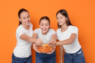 Photo of Group of happy teenage girls eating chips on orange background