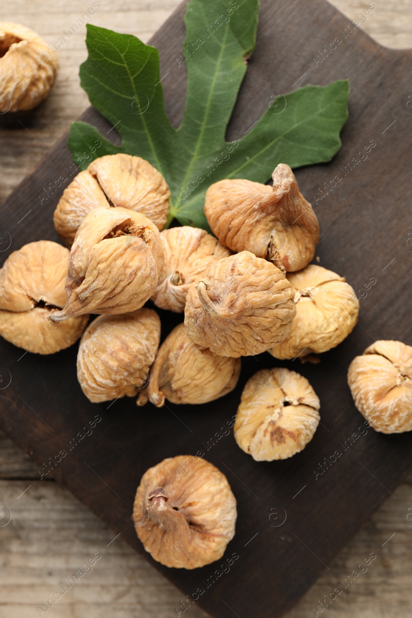 Photo of Board with tasty dried figs and green leaf on wooden table, flat lay