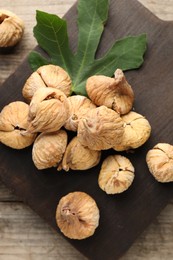 Photo of Board with tasty dried figs and green leaf on wooden table, flat lay