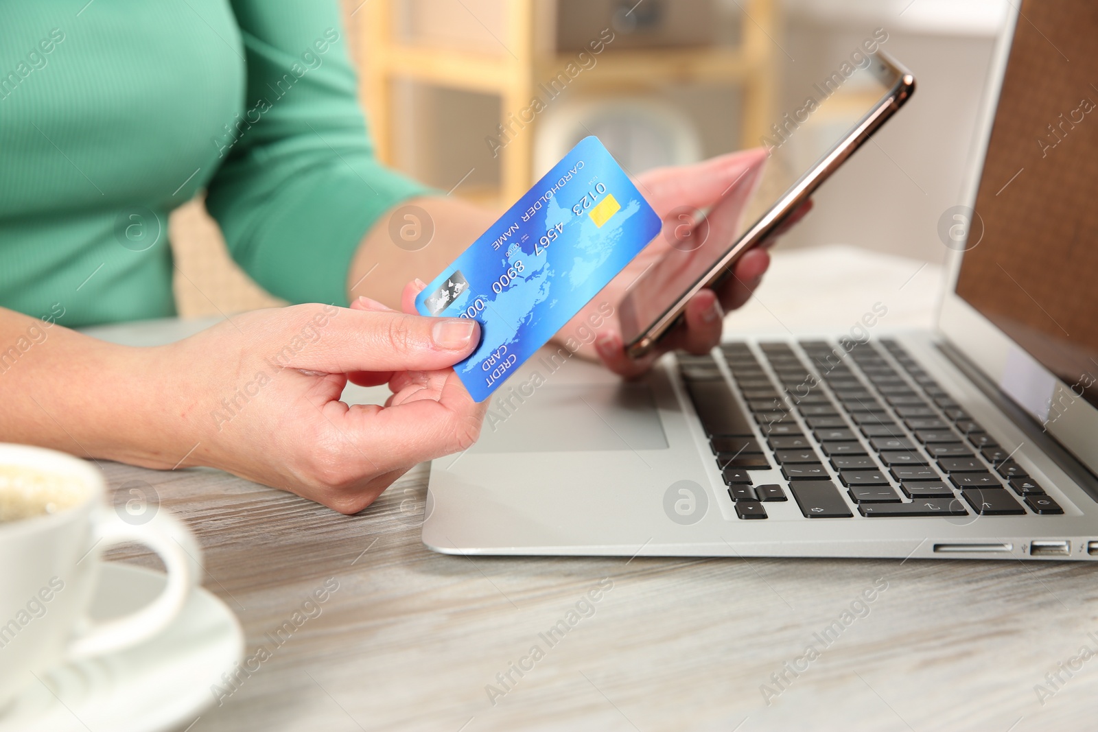 Photo of Online payment. Woman using credit card and smartphone near laptop at light wooden table indoors, closeup