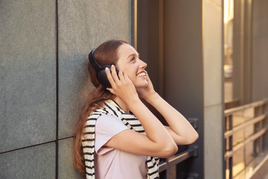 Photo of Happy woman in headphones enjoying music near building outdoors