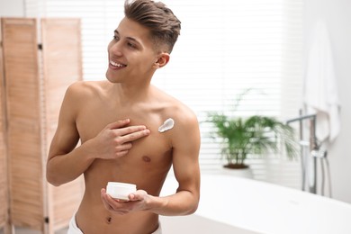 Photo of Handsome man applying moisturizing cream onto his shoulder in bathroom. Space for text
