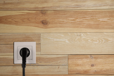 Image of Wooden wall with power socket and inserted plug, space for text. Electrical supply