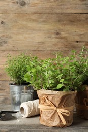 Different aromatic potted herbs, gardening tools and spool of thread on wooden table