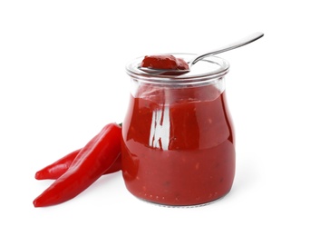 Photo of Glass jar with red sauce, spoon and fresh chili peppers on white background