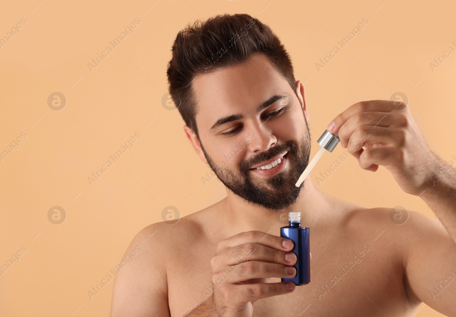 Photo of Handsome man with cosmetic serum in hands on beige background, space for text