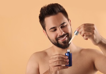 Handsome man with cosmetic serum in hands on beige background, space for text