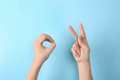 Woman showing word okay on color background, closeup. Sign language