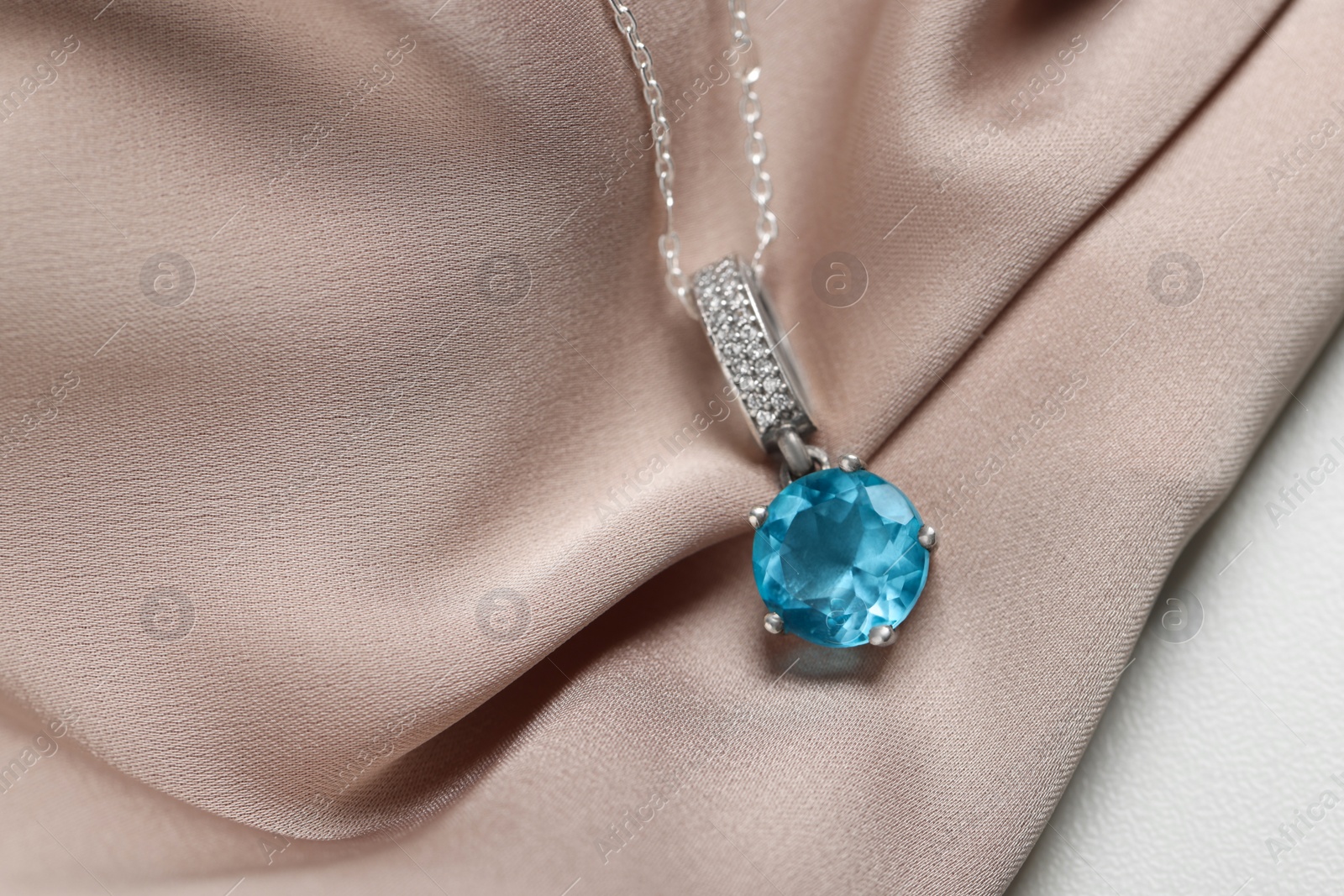 Photo of Beautiful necklace with light blue gemstone on beige fabric, closeup. Luxury jewelry