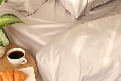 Photo of Tasty croissant and aromatic coffee near bed with stylish silky linens