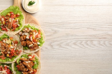 Photo of Delicious tacos with vegetables, meat and sauce on white wooden table, top view. Space for text