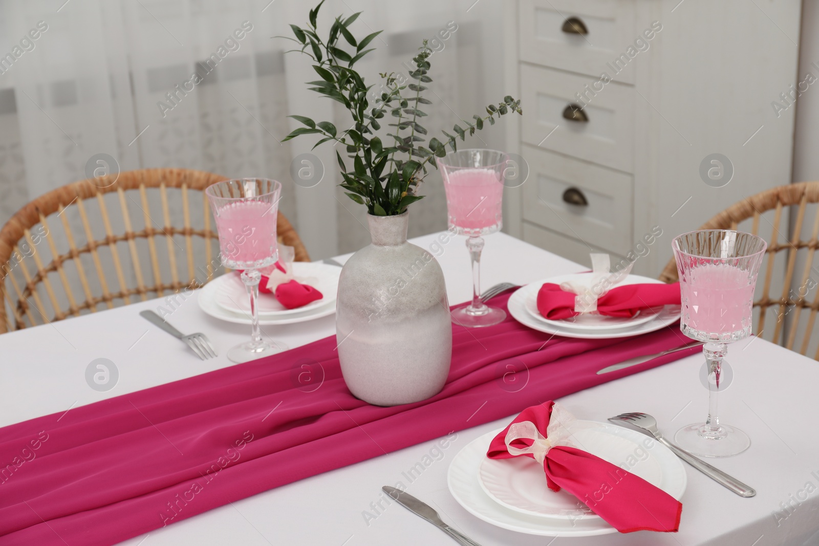 Photo of Table setting. Glasses of tasty beverage, plates, pink napkins and vase with green branches in dining room