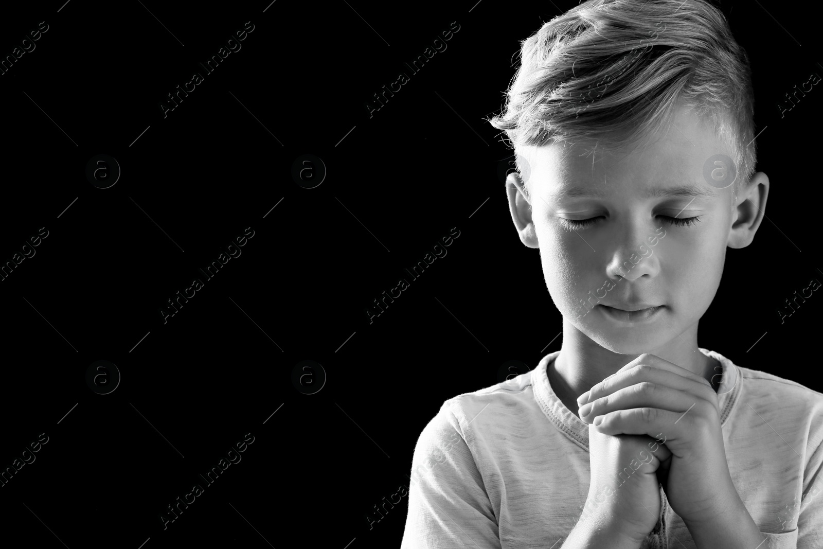 Photo of Little boy with hands clasped together for prayer on dark background, black and white effect. Space for text