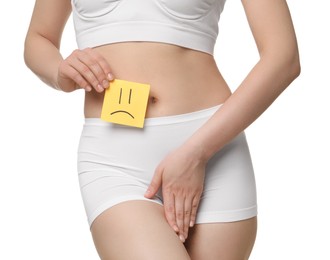 Photo of Woman holding sticky note with drawn sad face and suffering from cystitis on white background, closeup