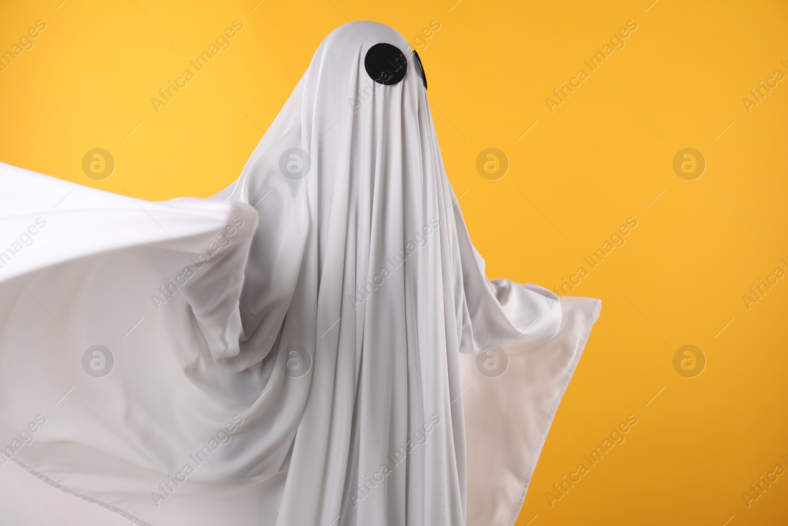 Photo of Creepy ghost. Person covered with white sheet on yellow background, space for text