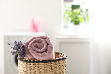 Photo of Wicker basket with rolled clean towel and lavender flowers indoors. Space for text