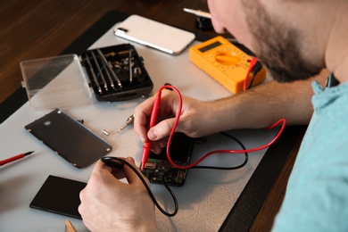 Photo of Technician checking mobile phone at table in repair shop, closeup