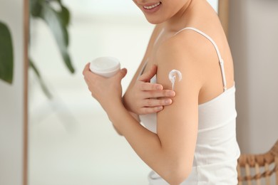 Photo of Young woman applying body cream on shoulder in room, closeup. Space for text