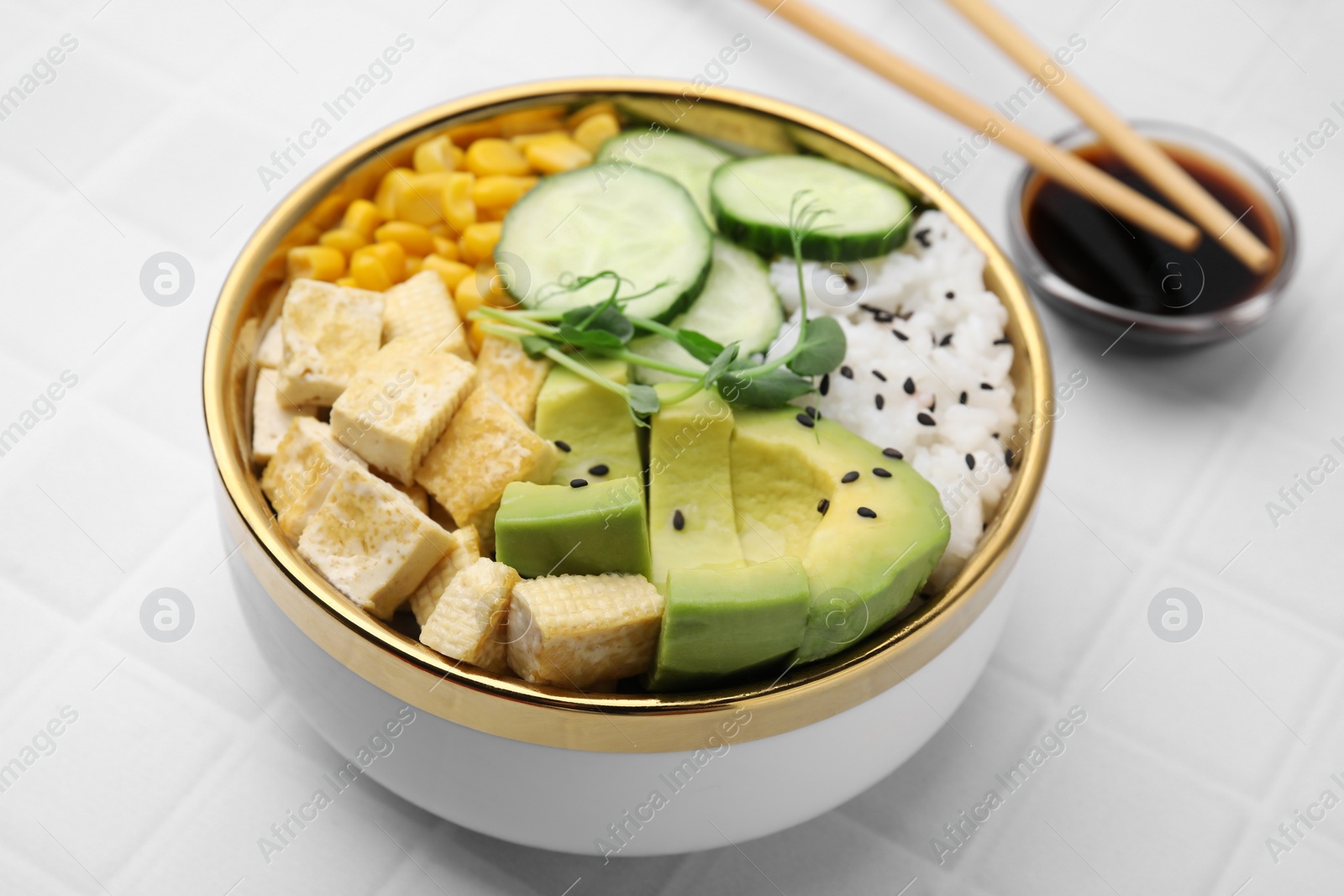 Photo of Delicious poke bowl with vegetables, tofu, avocado and microgreens served on white tiled table, closeup