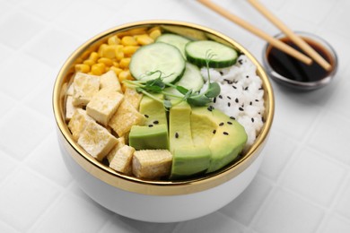 Delicious poke bowl with vegetables, tofu, avocado and microgreens served on white tiled table, closeup