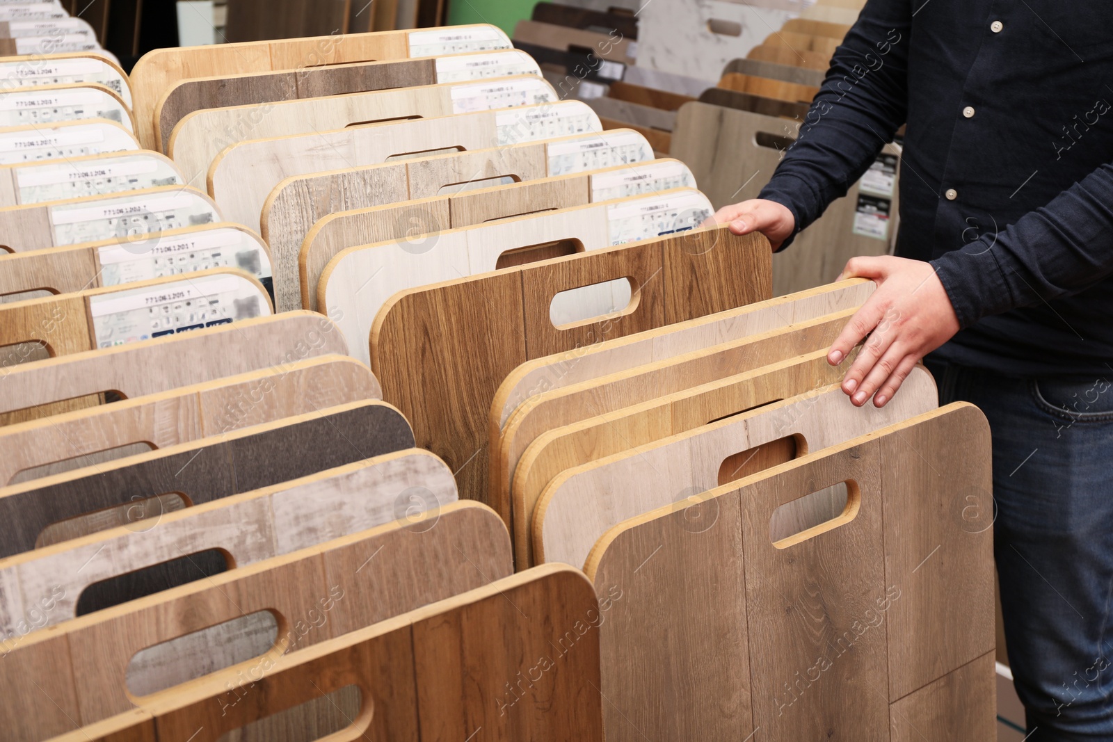 Photo of Man choosing wooden flooring among different samples in shop, closeup