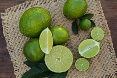 Photo of Fresh ripe limes and green leaves on wooden table, top view