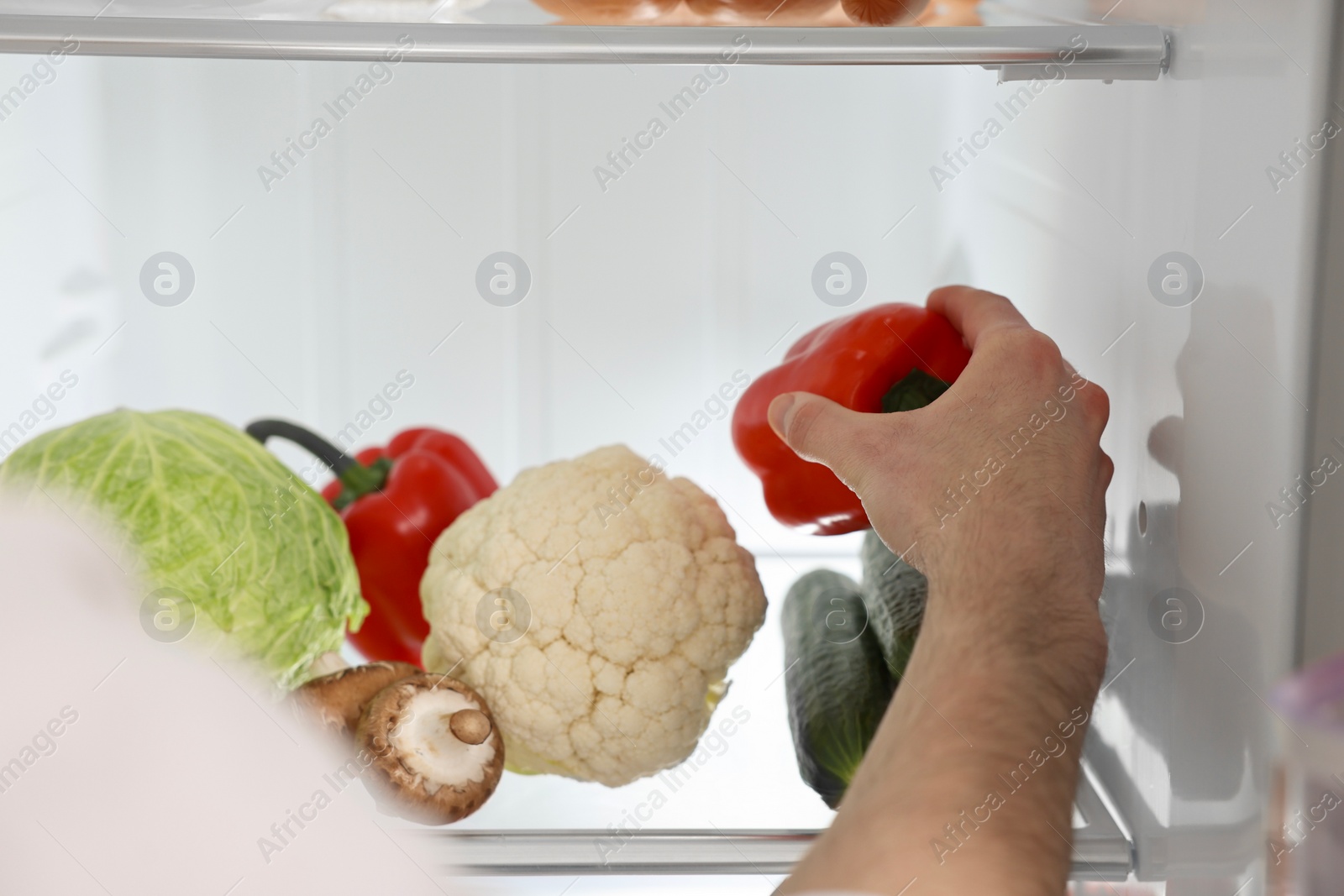 Photo of Man taking bell pepper out of refrigerator, closeup
