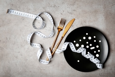 Plate with weight loss pills, cutlery and measuring tape on gray background, flat lay