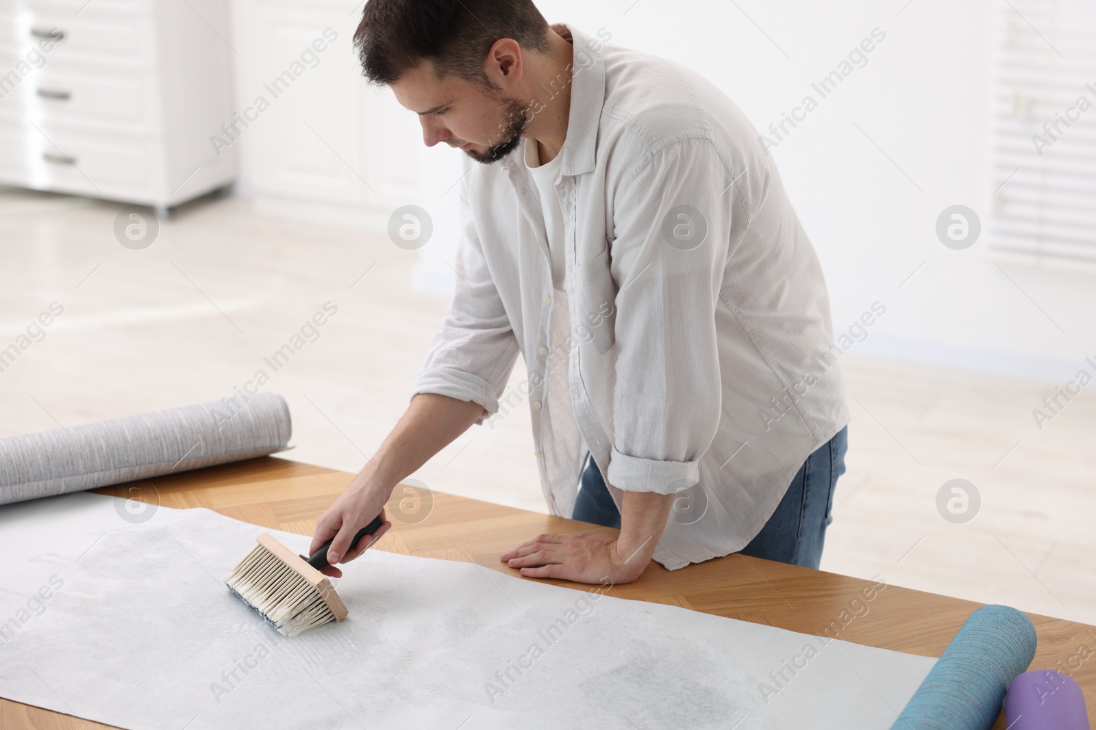 Photo of Man applying glue onto wallpaper sheet at wooden table indoors