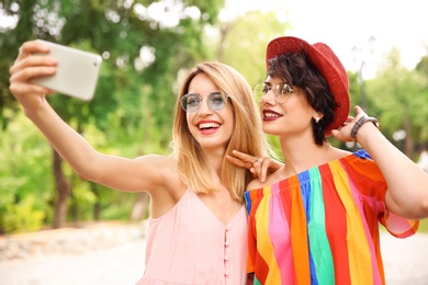 Young women in stylish clothes taking selfie outdoors