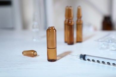 Photo of Open pharmaceutical ampoule with medication and syringe on white wooden table