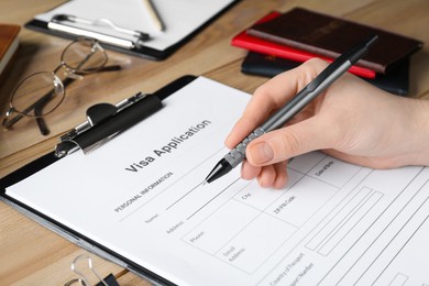 Woman filling visa application form at wooden table, closeup