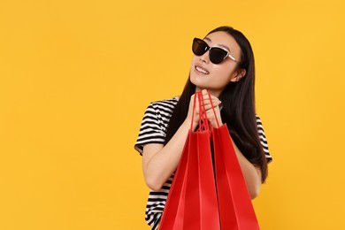 Smiling woman with shopping bags on yellow background. Space for text