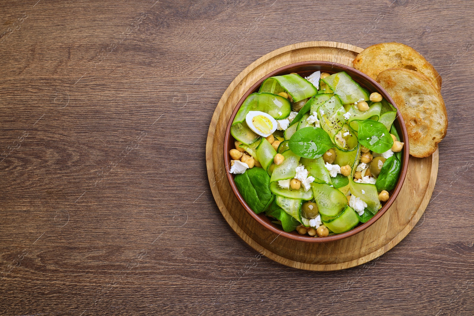 Photo of Bowl of delicious cucumber salad and toasted bread on wooden table, top view. Space for text