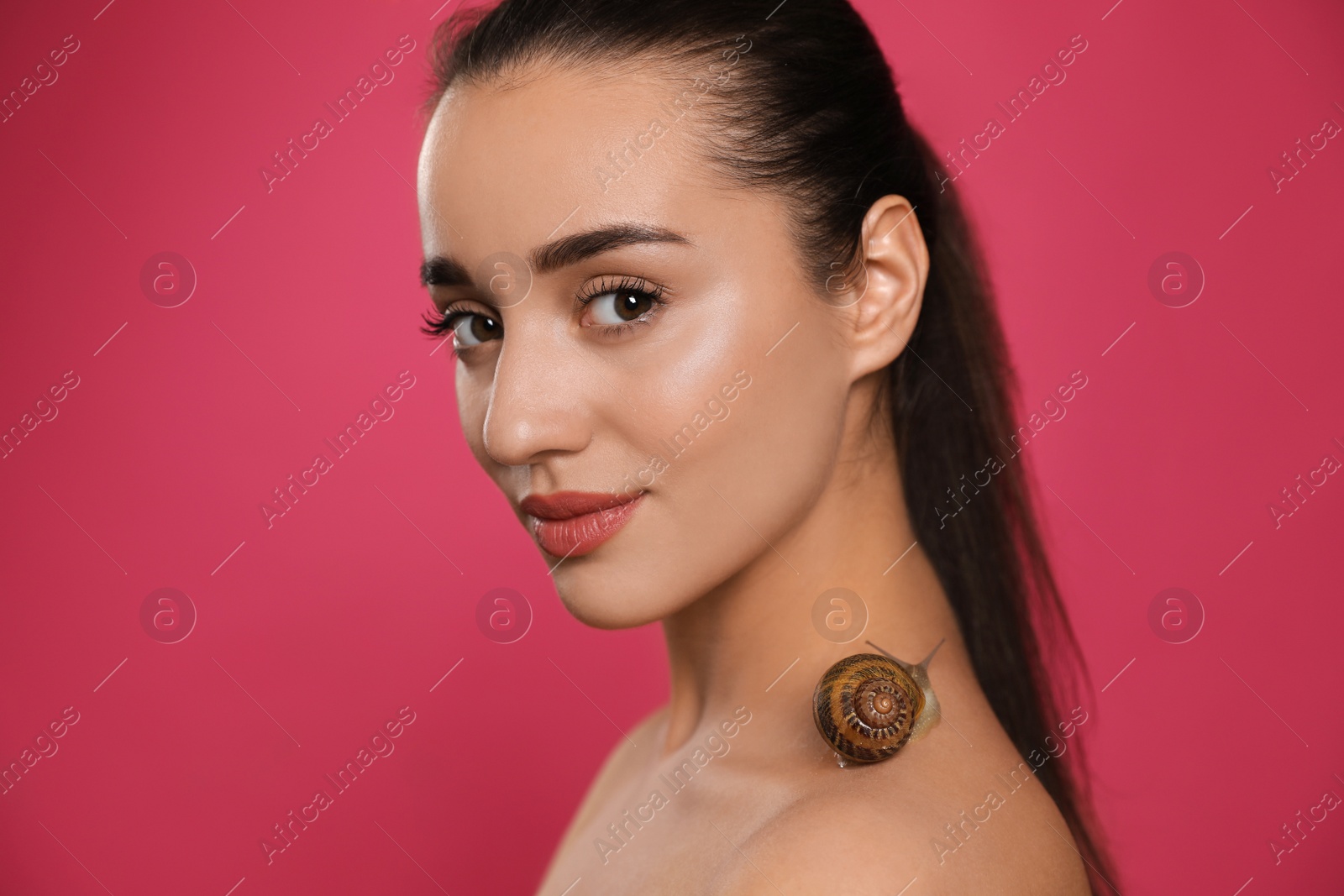 Photo of Beautiful young woman with snail on her neck against pink background