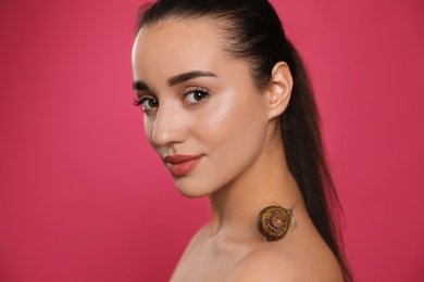 Beautiful young woman with snail on her neck against pink background