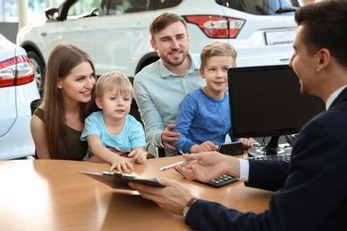 Photo of Young family with salesman sitting at table in dealership. Buying new car