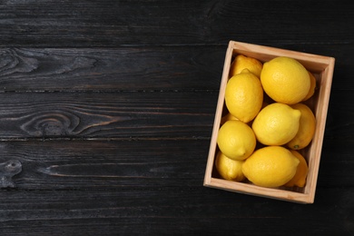 Photo of Wooden crate full of fresh lemons on dark background, top view. Space for text