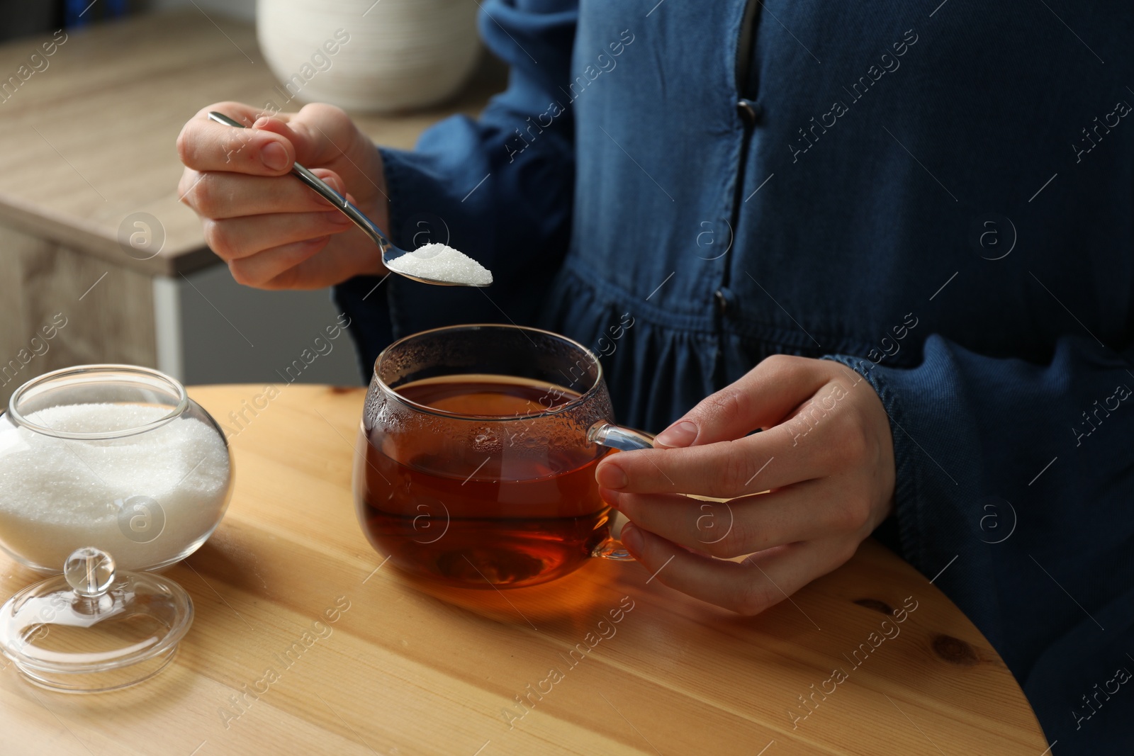 Photo of Woman adding sugar into aromatic tea at wooden table indoors, closeup