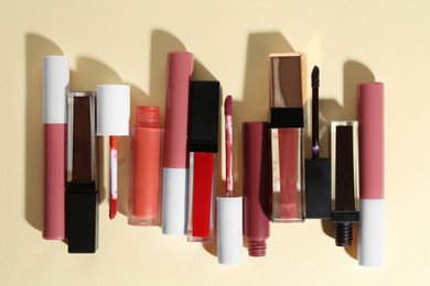 Photo of Different lip glosses and applicators on pale yellow background, flat lay