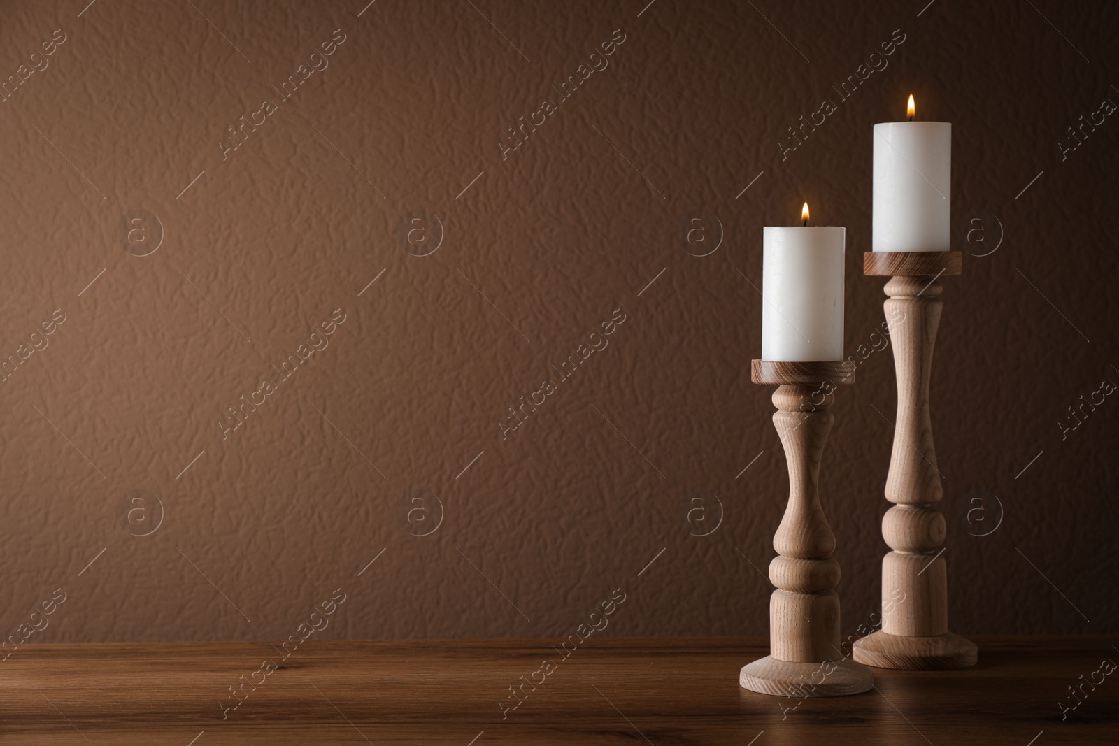 Photo of Elegant candlesticks with burning candles on wooden table. Space for text