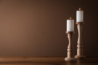 Elegant candlesticks with burning candles on wooden table. Space for text