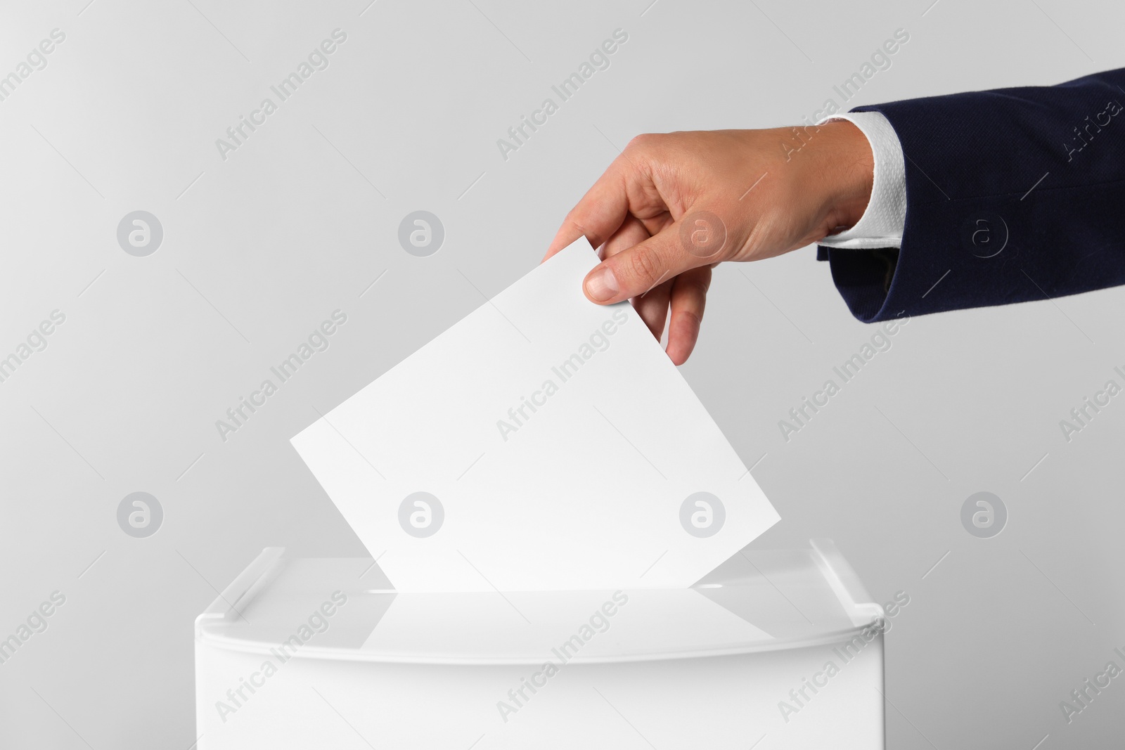 Photo of Man putting his vote into ballot box on light grey background, closeup