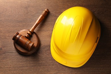 Photo of Law concept. Gavel and yellow hard hat on wooden table, top view